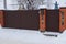 Brown gate and part of a metal and brick fence outside in white snow