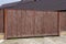 Brown gate of wooden planks and part of the fence on a rural street