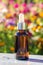 Brown glass dropper bottle with serum, essential oil or other cosmetic product on bright floral background. Natural Organic Spa