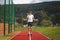 Brown-haired boy with an athletic figure wearing a white T-shirt and black shorts is jumping rope on an athletic oval. Training to