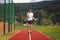 Brown-haired boy with an athletic figure wearing a white T-shirt and black shorts is jumping rope on an athletic oval. Training to