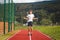 Brown-haired boy with an athletic figure wearing a white T-shirt and black shorts is jumping rope on an athletic oval. Training to