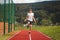 Brown-haired boy with an athletic figure wearing a white T-shirt and black shorts is jumping rope on an athletic oval. Training to