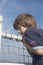 Brown-haired boy in t-shirt, hanging over the railing of a ferry and looking around, in the background a little rainbow