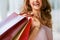 Brown-haired, happy, smiling woman holding up shopping bags