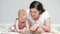 Brown-haired mother reads book to amused baby girl on floor