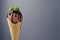 Brown ice cream in waffle cone with chocolate sauce, mint leaf on pastel grey background, closeup, details, top, half.