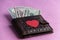 Brown leather wallet with a red heart on a pink background. Dollars stick out of the wallet. Close-up.