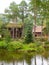 a brown log house and pond surrounded by trees and grass