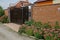 Brown metal gate and brick fence near decorative green plants and flowers