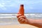 brown mockup sunscreen cream, lotion bottle in tanned male hand, sea waves in background, summer sun protection template scene