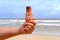 brown mockup sunscreen cream, lotion bottle in tanned male hand, sea waves in background, summer sun protection template scene