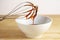 Brown molasses flows from a wire whisk into a white bowl, baking at home concept, wooden table and bright background