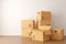 Brown moving storage cardboard boxes closed and open stacked in empty room in apartment or house with wooden floor with copy space