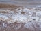 Brown muddy waves roll onto the shore with white foam, creating bizarre patterns.  Muddy surface of seawater due to strong wind