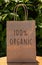 Brown paper bag with `100% Organic` message in front of a green leafy background