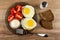 Brown plate with pieces of tomato, bowl of mayonnaise, fried eggs, fork, salt and slices of bread on wooden table. Top view