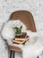 Brown soft loft style chair, fur rug, stack of books, bunch of chrysanthemums on light wall background. Interior concept, copy