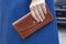 Brown stitched wallet in a female hand close-up on a background of blue coat