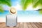 Brown straw hat and suitcase on wooden table with blurred sea,blue sky and palm tree background with copy space.