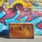 Brown suitcase in front of graffiti covered wall