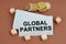 On a brown surface are coins, cubes and a business card with the inscription - GLOBAL PARTNERS