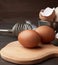 Brown whole chicken eggs on a wooden board, behind a whisk for whipping