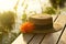 Brown woman hat with orange flower on wood terrace on morning natural sunlight water lake background