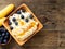 Brown wooden Bowl of homemade curd with banana, jam, blueberries on dark brown wooden background, top view, copy space