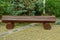 A brown wooden log bench stands on a gray sidewalk