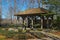 A brown wooden pergola with black metal tables and chairs surrounded by colorful flowers and lush green trees and plants