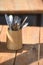 Brown wooden storage box on a wooden tabletop, filled with an array of kitchen utensils and spoons