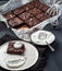 Brownie with ginger, dark chocolate coloured, cut into equal squares on the gray table. A piece of brownie lies on a