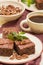 Brownie sweet chocolate dessert with walnuts and meant leaves on craft plate and cup of black coffee.