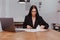 Brunette auditor in black suit working with documents on laptop in contemporary office or cafe.