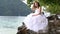 brunette beautiful bride sits on rock smiles