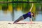 Brunette in blue sports shirt on fitness mat doing exercises on beach. Woman doing fitness exercise outdoors