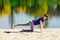 Brunette in blue sports shirt on fitness mat doing exercises on beach. Woman doing fitness exercise outdoors