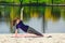 Brunette in blue sports shirt on fitness mat doing exercises on beach. Woman doing fitness exercise outdoors