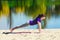 Brunette in blue sports shirt on fitness mat doing exercises on beach. Woman doing fitness exercise outdoors