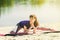 Brunette in blue sports shirt on fitness mat doing exercises on beach. Woman doing fitness exercise outdoors