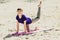 Brunette in blue sports shirt on fitness mat doing exercises on beach. Woman doing fitness exercise outdoors