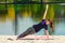 Brunette in blue sports shirt on fitness mat doing exercises on beach. Woman doing fitness exercise outdoors