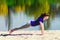 Brunette in blue sports shirt on fitness mat doing exercises on beach. Woman doing fitness exercise outdoors