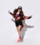 Brunette in a cap and a long bomber jacket, sneakers and long socks jumps, has fun, shows her tongue on a light wall with a shadow