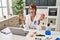 Brunette dentist woman holding apple and chocolate doughnut angry and mad screaming frustrated and furious, shouting with anger