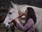 Brunette female playing a native american flute with a white portuguese horse by her side.