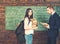 Brunette female student standing in front of green board with heap of books and huge backpack. Professor looking at