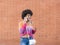 Brunette girl with casual style, glasses and afro hair talks happily by her smarphone in front of a brick wall
