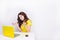 A brunette girl with curly hair looks frustrated sitting in front of laptop in yellow case. She sits behind white table